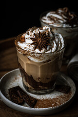 Two glasses of Pumpkin pie spice mocha latte with whipped cream and dark chocolate on plate on wooden tray on dark background .