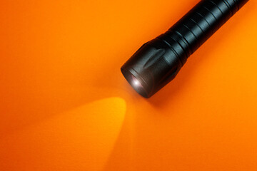 Black Flashlight and a ray of light on the orange background. Close up photo.