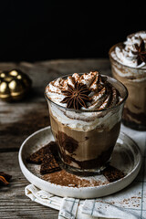 Two glasses of Pumpkin pie spice mocha latte with whipped cream and dark chocolate on plate on wooden table on dark background .