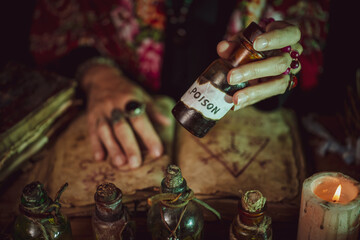 Female witch making potion on dark background, magic bottles with potions and candles on table of alchemist, Halloween theme