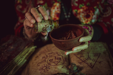 Female witch making potion on dark background, magic bottles with potions and candles on table of...