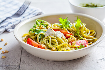 Spaghetti pasta with pesto sauce, olives, tomatoes and pine nuts in white bowl. Italian cuisine concept.