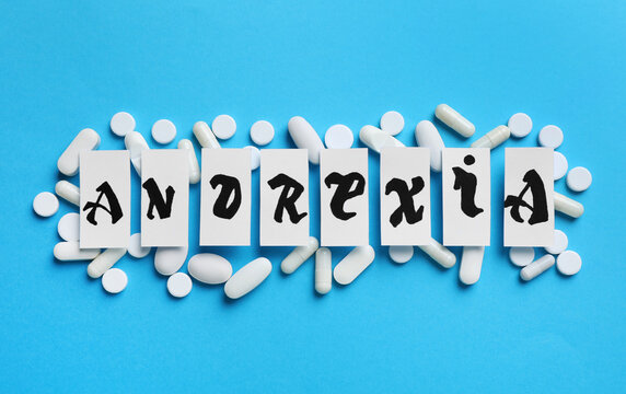 Pills and word Anorexia made of paper pieces on light blue background, flat lay