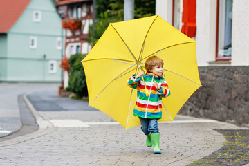 Little toddler boy playing with big yellow umbrella on rainy day. Happy positive child running...