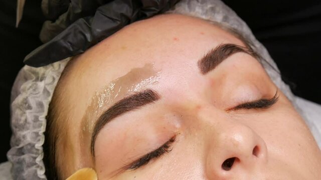 Correction of a beautiful aesthetic shape of eyebrows with hot wax and special tweezers. Removing unnecessary hair from the face.