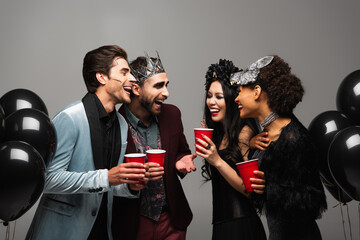 happy multiethnic friends talking and laughing on halloween party isolated on grey