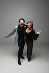 excited african american woman in werewolf mask waving hand near laughing man on grey