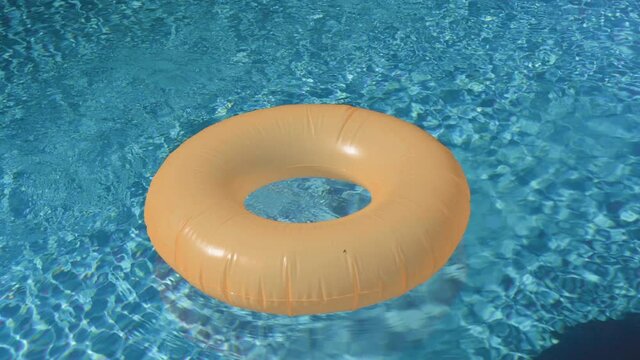 A bright orange swim in a blue pool, ring in a refreshing blue pool with waves reflecting in the summer sun. Active leisure background.