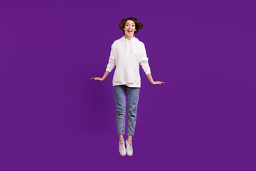 Full size photo of young attractive lovely girl jumping wear white sweater and jeans isolated on violet color background