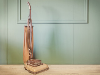 Vintage brown vacuum cleaner in an empty room with green wall and wooden floor - obrazy, fototapety, plakaty