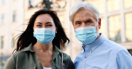 Fototapeta na wymiar Fathers daughter. Portrait view of the happy brunette woman and her father wearing protective masks looking at each other and at the camera while walking at the city during pandemic