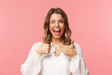 Portrait of sassy good-looking blond girl assure all good, show thumbs-up and wink with classy pleased smile, recommend visit place, shop at online store, standing in white dress pink background - obrazy, fototapety, plakaty