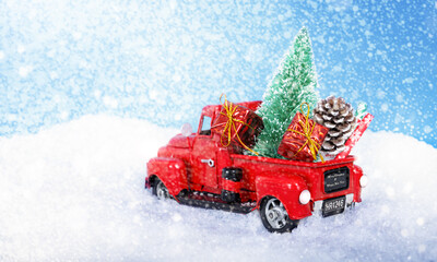 Red truck with gifts and a Christmas tree in the snow. Blue background.