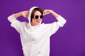 Photo of sweet charming young woman dressed white pullover dark glasses dancing empty space smiling isolated violet color background