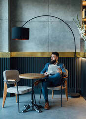 Handsome Businessman Reading Newspaper in a Cafe.
 
Serious elegant business man with a newspaper sitting in a restaurant and looking away. 
