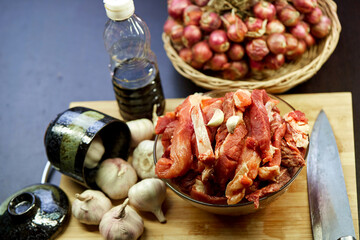 fresh raw meat on cutting board with ingredients for cooking in kitchen