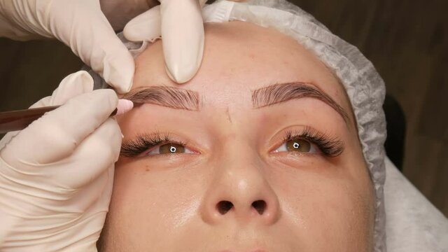 The master draws a new shape of the eyebrows with special pencil in white gloves. Eyebrow shape correction. Microblading, permanent makeup, tattoo