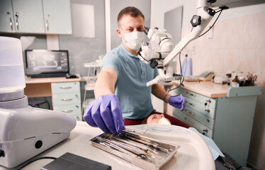 Close up of male dentist hand in sterile glove holding metal dental explorer. Stomatologist taking...