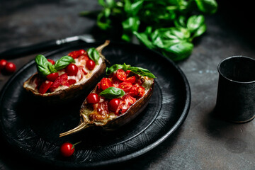 Eggplants with tomatoes, basil and cheese on a black plate