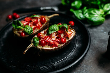 Eggplants with tomatoes, basil and cheese on a black plate