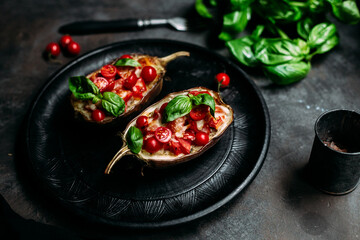Eggplants with tomatoes, basil and cheese on a black plate