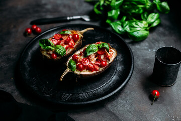 Eggplants with tomatoes, basil and cheese on a black plate