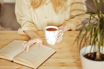 woman in yellow shirt with cup of coffee and book on wooden table