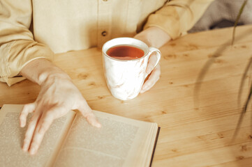 woman in yellow shirt with cup of coffee and book on wooden table