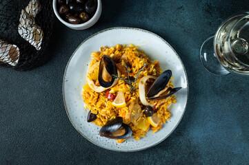 Classic dish of Spain, seafood paella in plate on blue background top view. Spanish paella with shrimps, clamps, mussels and fresh lemon. Spanish food. Comfort food. Rice with seafood.
