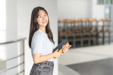 Front view portrait of a young cheerful Asian adolescent woman college student in relaxed casual back to school carry books stands in campus building