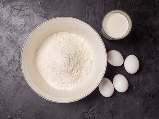 Flour, milk and eggs on a black background. Pancake baking ingredients. View from above