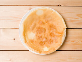 Round pancake in a white plate on a wooden background. View from above