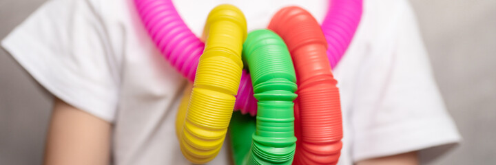 anti stress sensory pop tube plastic toy in kid's hands. a little happy child boy plays with a poptube fidget toy at home. children holding and playing pop tube multicolored colors. banner