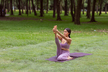 Mexican woman doing yoga exercises in the park on green grass