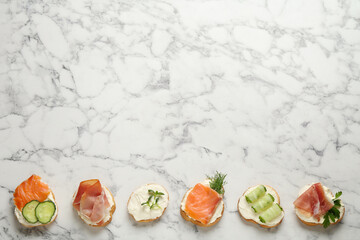 Delicious sandwiches with cream cheese and other ingredients on white marble table, flat lay. Space for text