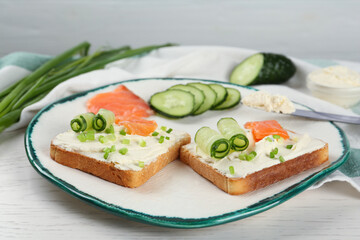 Fototapeta na wymiar Toasted bread with cream cheese, salmon and cucumber on white wooden table
