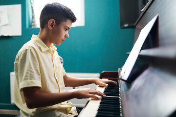 Boy practicing playing the piano at home