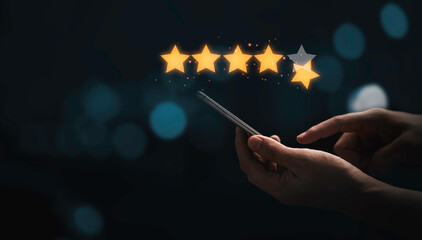 Hand holding and using smartphone with virtual five golden stars with glowing light for the best...