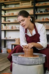female ceramist artisan works behind potter's wheel and sculpts handmade earthenware