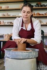 female ceramist artisan works behind potter's wheel and sculpts handmade earthenware