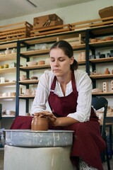 female ceramist artisan works behind potter's wheel and sculpts handmade earthenware