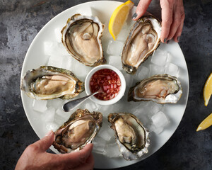 Plate of six oysters in the half shell served on ice, Mignonette Sauce and two hands reaching for...