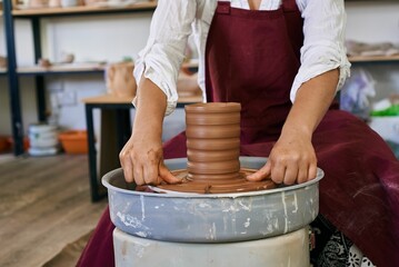 female ceramist artisan works behind potter's wheel and sculpts handmade earthenware