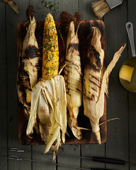 Four corn cob in husks cooked on BBQ on wooden table