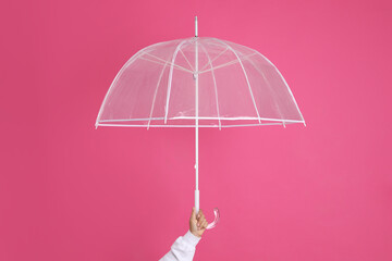 Woman with open transparent umbrella on pink background, closeup