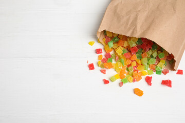 Overturned paper bag with mix of delicious candied fruits on white wooden table, flat lay. Space for text