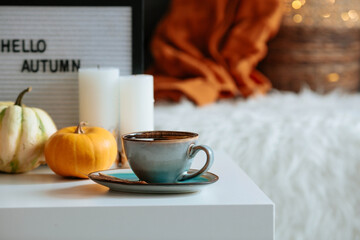 Still-life. A blanket, pumpkins and a cup of tea on the coffee table in the home interior of the living room. A cozy autumn concept.