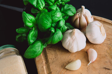 Garlic bulbs on a wooden board on a black background, with dried garlic and a bunch of basil. Diet. Condiments and spices for Mediterranean cuisine.
