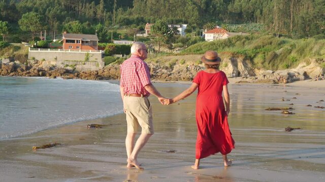 Anonymous senior couple standing on beach by waving sea