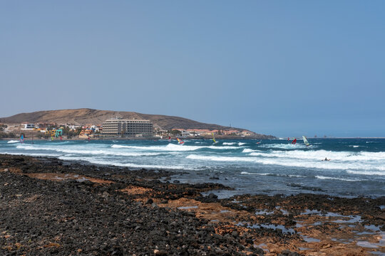 Summer views of the eastern coast of the town towards Montana Pelada with surfers practicing water sports such as surfing and windsurfing, El Medano, Tenerife, Canary Islands, Spain